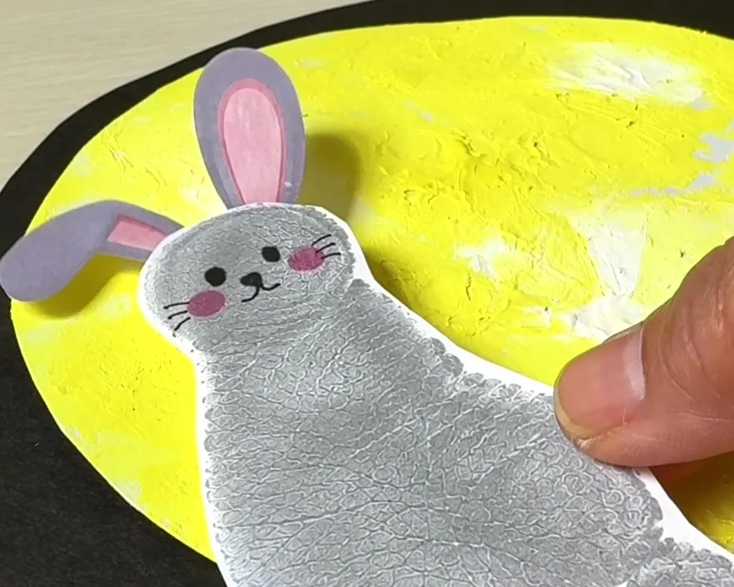 月に見立てた画用紙の上に足形で作ったウサギを貼り付けている画像