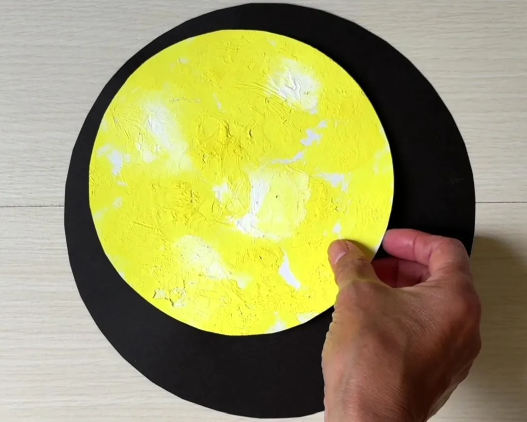 丸く切った黒い画用紙の上に黄色と白の絵の具を塗った画用紙を重ねている画像