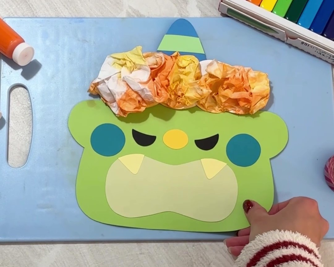 画用紙で作った鬼の顔に先ほどの色付きの半紙を貼り付けている様子