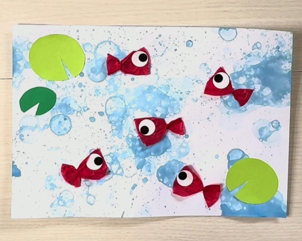 先ほどのシャボン玉液を吹きかけた台紙に花紙で作った金魚を貼り、画用紙で作った浮草を貼った画像