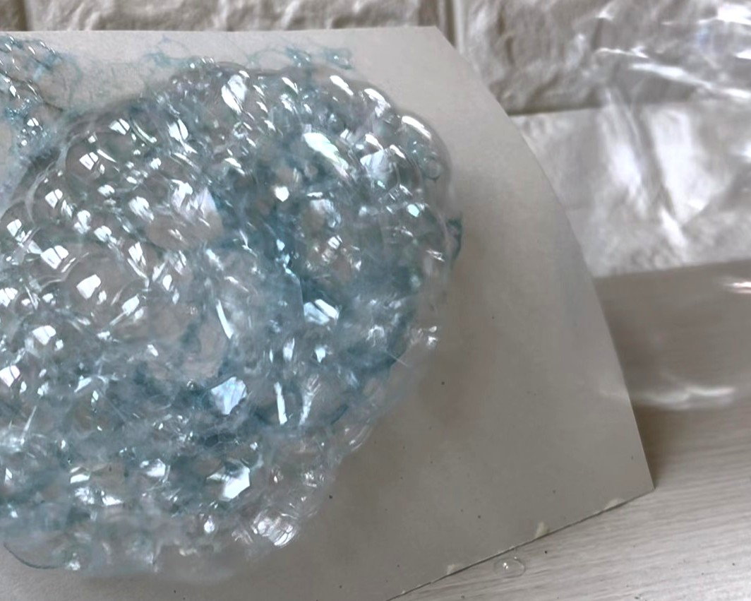 作った道具を先ほどのシャボン玉液につけ、画用紙に向かって息を吹いている様子